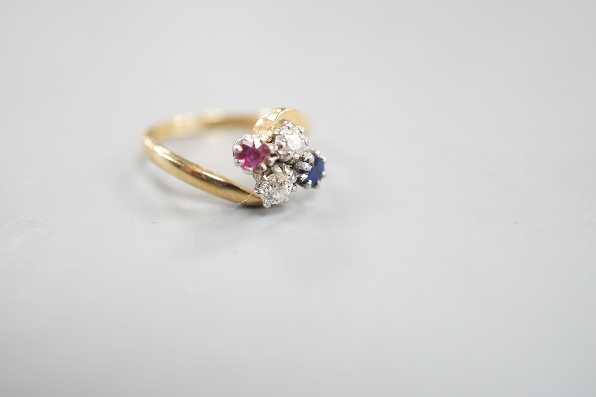 An early 20th century 18ct & plat, ruby, sapphire and diamond set four stone crossover ring, size M, gross weight 4 grams.